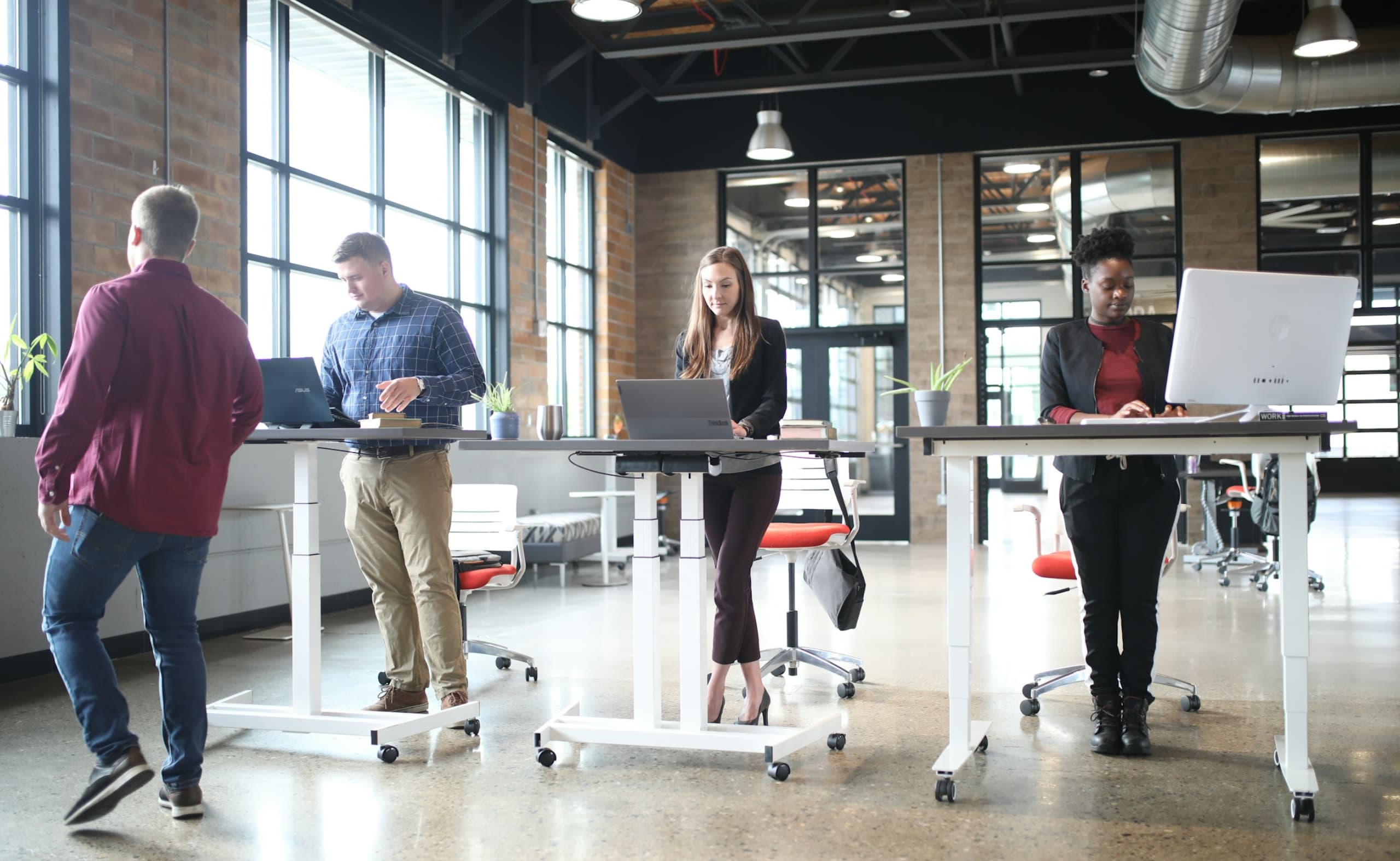 Group of professionals using standing desks near large windows in a modern office.