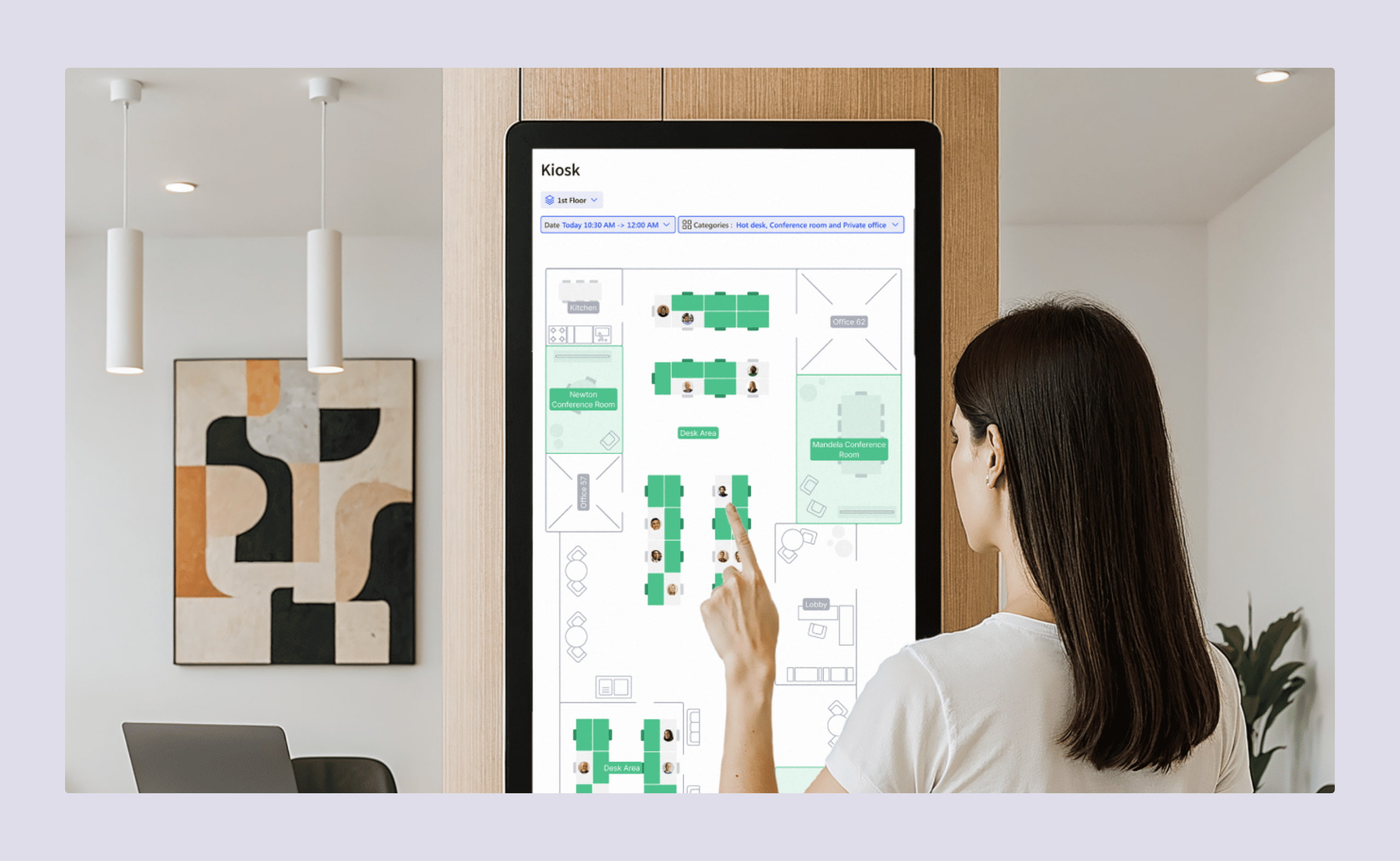 A woman using a touchscreen kiosk to view a digital office floor plan and desk availability.