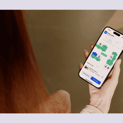 Person holding a smartphone with Archie’s desk booking app open, showing a digital office floor plan and available desks.