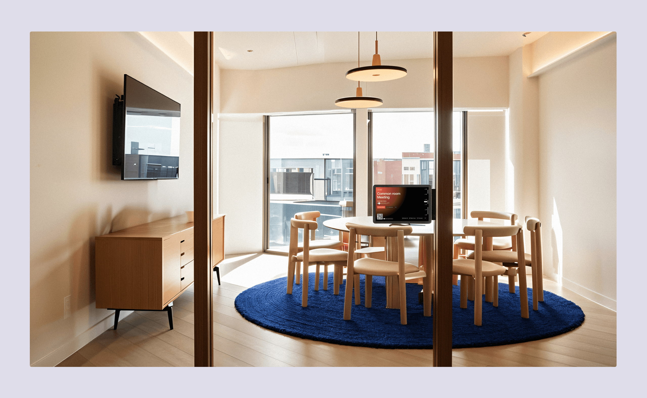 Small modern meeting room with wooden chairs around a round table, digital room display showing booking details, and large windows with city views.